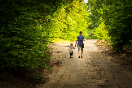 Mother and child walking by forest path with holding hands. Summer forest and family.の写真素材