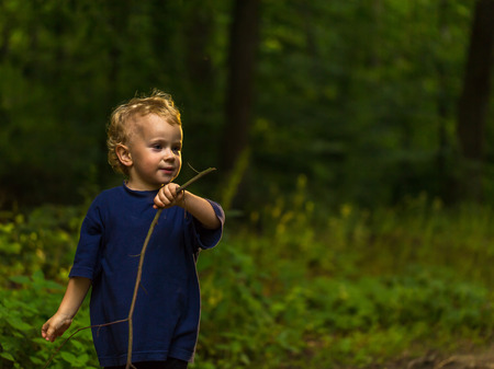 Small blonde boy playing in forest. Natural landscape with small caucasian boy.の写真素材