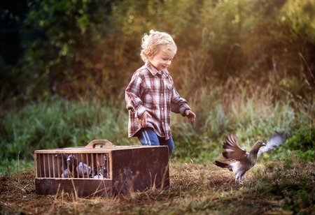 Boy playing outdoor in autumn or spring scenery with flying pigeons.の写真素材