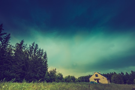 Vintage photo of storm sky over meadow, house and forest.の写真素材