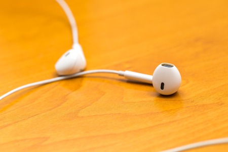 Close up of white headphones lying on wooden table. Small white earphones.の写真素材
