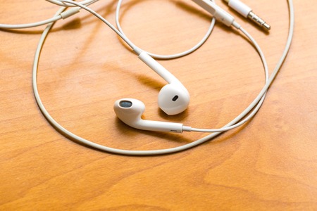 Close up of white headphones lying on wooden table. Small white earphones.の写真素材