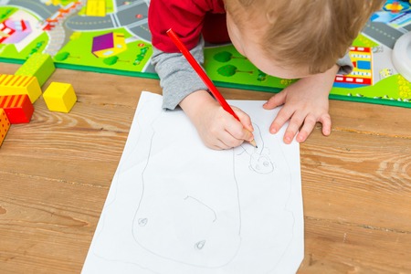 Little child drawing with pencil on white paper. Close up of toddler playing on floor.の写真素材