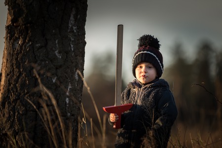 Young boy playing outdoor with wooden sword. Autumnal landscape and young boy.の写真素材