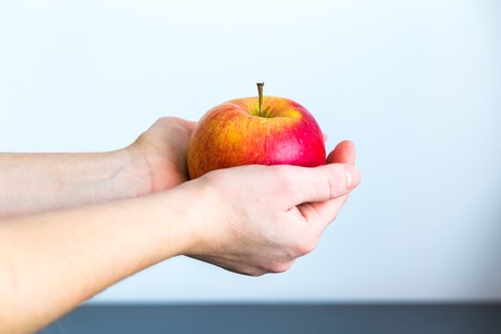 Girl holding red apple against white wall. Close up of fresh fruit.の写真素材