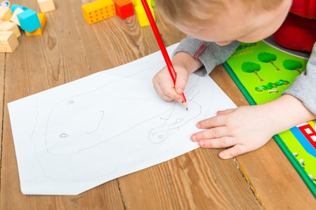 Little child drawing with pencil on white paper. Close up of toddler playing on floor.の写真素材