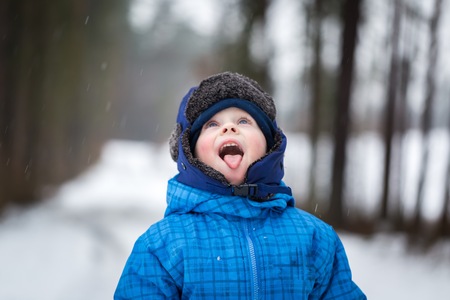 Happy little boy playing outdoor in winter snow- boy catching falling snow with his tongue. Snowy weather and caucasian child.の写真素材