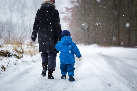 Mother and baby walking by sandy forest road in wintertime. Snowy weather and caucasian family.の写真素材