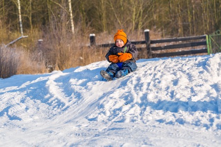Happy little caucasian boy downhill on plastic slider or sledge. Winter child outdoor activity.の写真素材