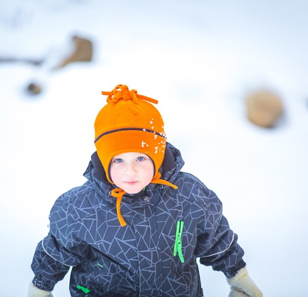 Happy boy playing outdoor in winter. Caucasian child in orange hat and warm clothes playing outdoor in winter.の写真素材