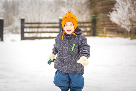 Happy boy playing outdoor in winter. Caucasian child in orange hat and warm clothes playing outdoor in winter.の写真素材