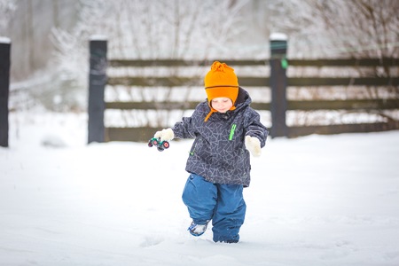 Happy boy playing outdoor in winter. Caucasian child in orange hat and warm clothes playing outdoor in winter.の写真素材