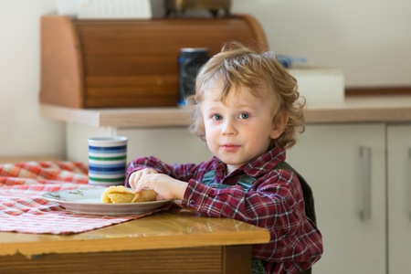 Boy eating pancake at the table. Blonde caucasian boy sitting at the kitchen table and eating.の写真素材
