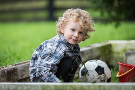 Young caucasianboy with curly hair playing in sandbox. Baby digging in sand.の写真素材
