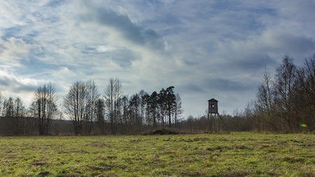 Meadow landscape with raised hide and trees under beautiful cloudy sky.の写真素材