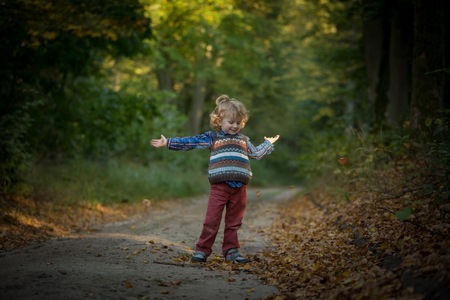 Young blonde boy with long curly hair playing in outdoor in autumnal forest.の写真素材