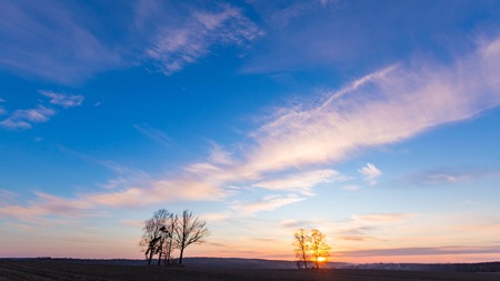 Beautiful evening colorful sky over plowed fields and trees, typical european village landscape.の写真素材