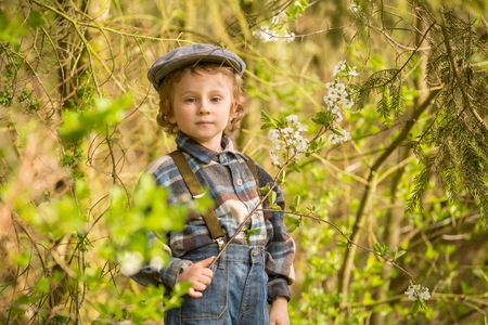 Young blonde boy posing in blooming orchard in springtime.の写真素材