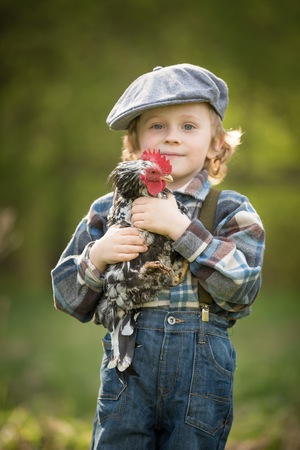 Small boy portrait with chicken. Caucasian curly haired boy in hat holding small chicken in outdoor.の写真素材
