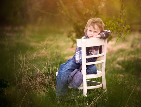 Young blonde boy relaxing on white old chair standing under birch tree in outdoor.の写真素材