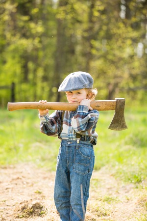 Small caucasian boy in hat posing with big axe. Portrait of small lumberjackの写真素材