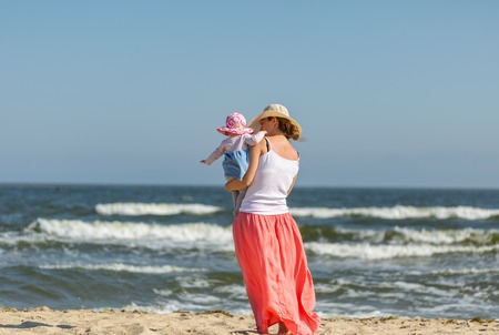 Mother with small baby girl relaxing on sea beach at sunny summer day.の写真素材