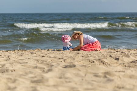 Mother with small baby girl relaxing on sea beach at sunny summer day.の写真素材