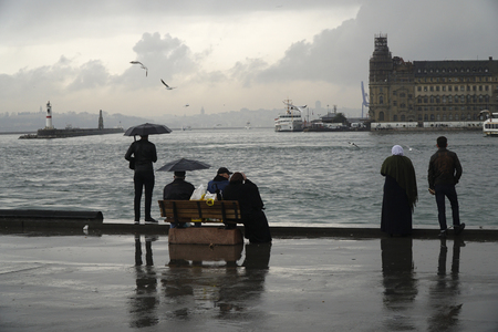 Istanbul, Turkey - March 8, 2018 : Rainy day at The Istanbul, Kadikoy seaside. Some people are watching The Istanbul Landscape with The Haydarpasa Train Station Building and jetty with lighthouse.のeditorial素材