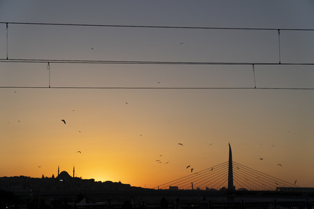 Historical and modern architecture together At Istanbul Sunset. There is a historical mosque at the left side and The Subway Bridge at the right side of the image. There are cables of trams at the top.の写真素材