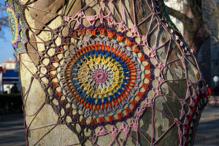 Spectacular handmade colorful knitted ornament on a tree trunk.