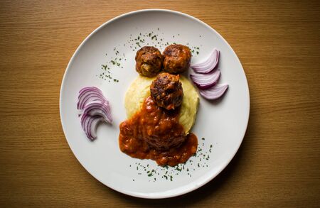 Mashed potato with meatballs in tomato sauce on white plate on wooden backgroundの写真素材