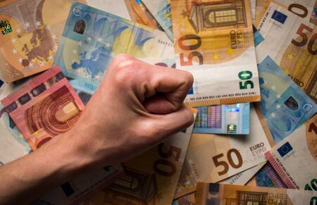 Woman tight fist on paper money, euro banknotes backgroundの写真素材