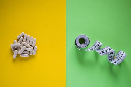 Medical pills and tape measure on yellow and green divided background. Healthy lifestyle conceptの写真素材