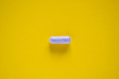 One white medical pill on yellow backgroundの写真素材