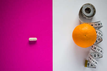 Medical pill opposite orange fruit with tape measure on pink and white divided backgroundの写真素材