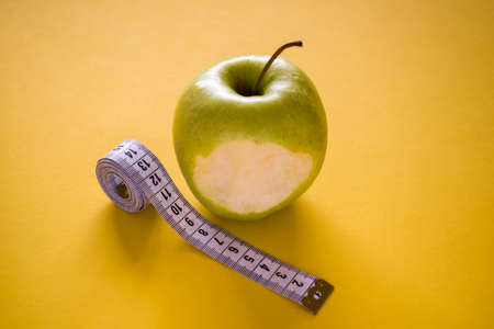 Bitten apple and measuring tape on yellow backgroundの写真素材