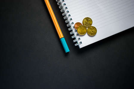 Cut out pen and notepad on black background with coinsの写真素材