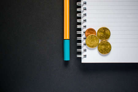 Cut out yellow pen and notepad with coins on black backgroundの写真素材