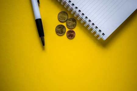 Pen, coins and notepad on yellow backgroundの写真素材