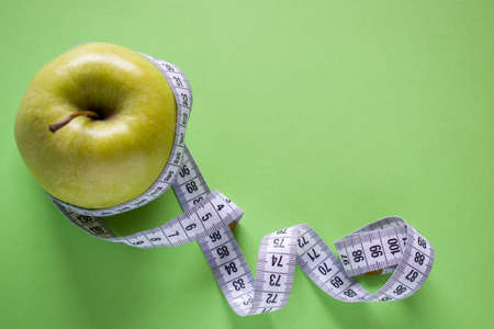 Apple wrapped with measuring tape on green background