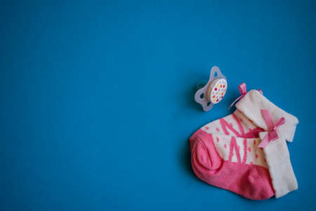 Pink baby socks and pacifier on blue background with copy space
