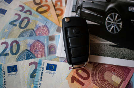Folded black car key and cut out car catalog on euro money banknotes