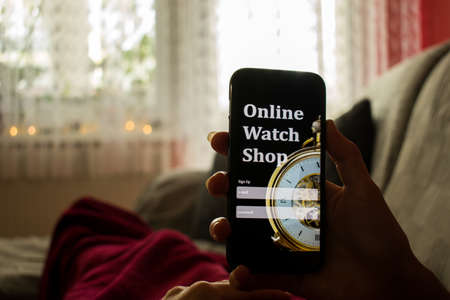 Woman lying in bed with smartphone searching for online watch shop. Online buying concept