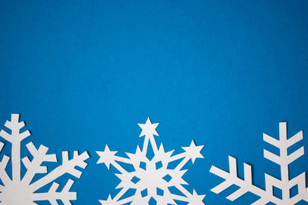 Blue colored paper background with white handmade snowflakesの写真素材