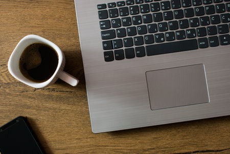 Laptop, cup of coffee and smartphone on wooden desk, flat lay. Work from home, office concept