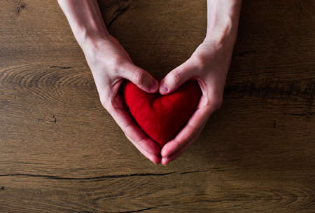 Red heart in woman hands on wooden backgroundの写真素材