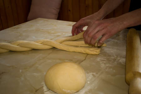 Female woman hands preparing braided dough for baking, close up. Dough, rolling pin on kitchen tableの写真素材