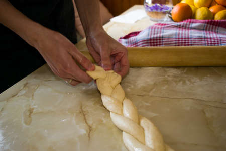 Female hands braiding dough on a kitchen table. Close upの写真素材