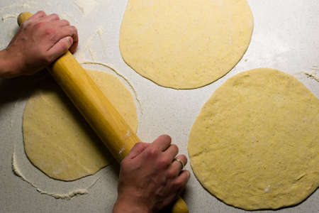Top view of female hands kneading dough with wooden rolling pinの写真素材