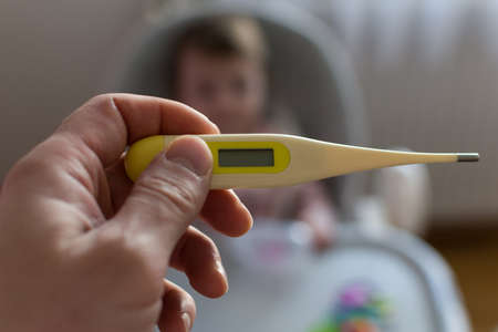 Close-up of hand holding thermometer. Sick child with high fever and fathers hand holding...